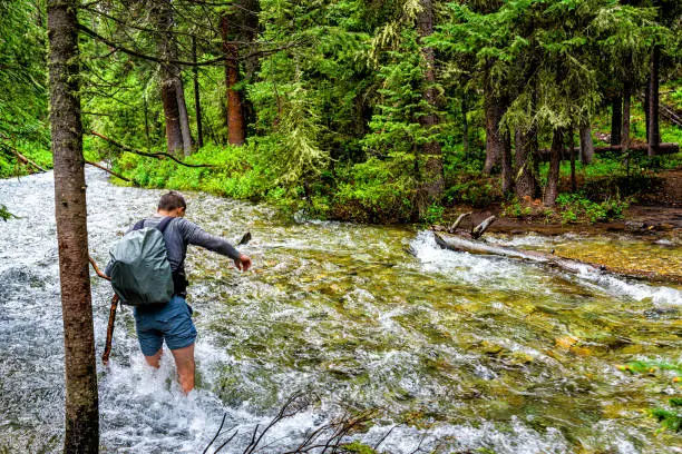 Man crossing fording river on Conundrum Creek Trail in Aspen, Colorado in 2019 summer in forest woods with strong current and deep water