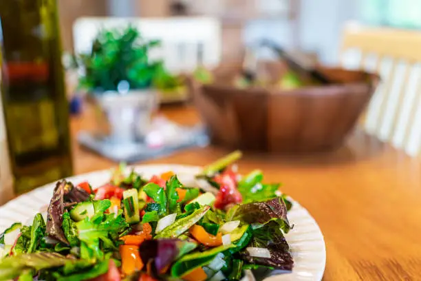 Closeup of plate with fresh green mixed lettuce salad in bowl background with bell peppers in rustic dining room wooden table