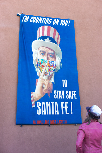 Santa Fe, NM: A woman looking at a banner promoting mask wearing; the banner in downtown Santa Fe shows Uncle Sam wearing a protective COVID-19 mask.