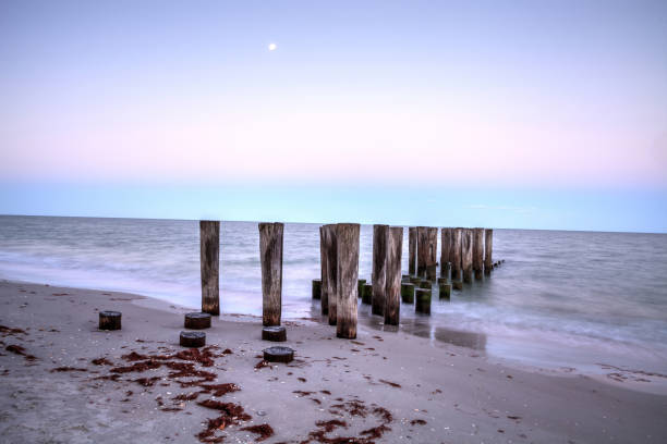 Dilapidated pier leading into the ocean on the beach Dilapidated pier leading into the ocean on the beach of Port Royal in Naples, Florida at sunrise as the full moon sets. naples beach stock pictures, royalty-free photos & images