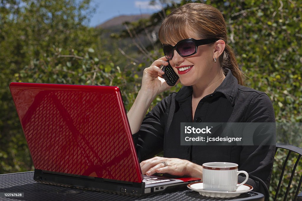 Sonriente mujer de negocios hablando por un teléfono móvil y portátil. - Foto de stock de Adulto libre de derechos