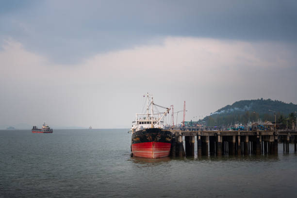 Ranong/Thailand - March 2020 : A cargo vessel is wharf at the local shipping dock, whit background of blue cloudy sky in the evening time. Heavy transportation and logistic industrial editorial photo.