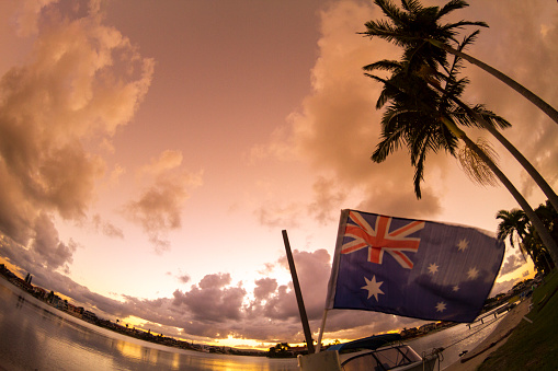 Sunset canal landscape in Broadbeach / Mermaid Waters, Gold Coast, Queensland, with backlit palm trees and an Australian flag.