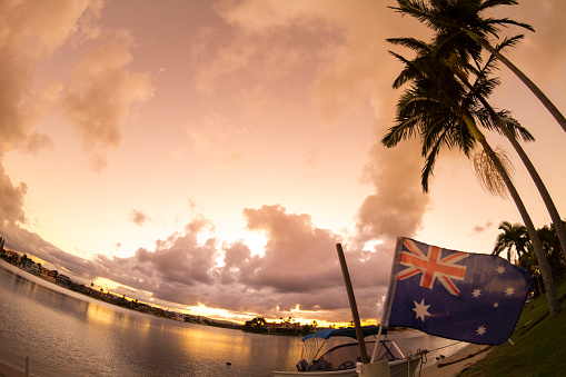 Sunset canal landscape in Broadbeach / Mermaid Waters, Gold Coast, Queensland, with backlit palm trees and an Australian flag.