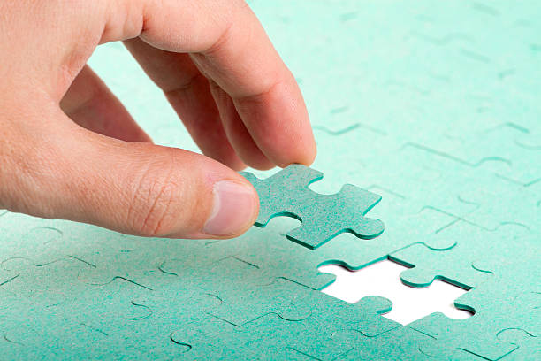 Hand inserting piece of green jigsaw puzzle into the hol stock photo