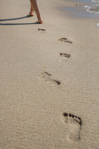 Woman walking barefoot on the sandy beach leaving foot prints behind