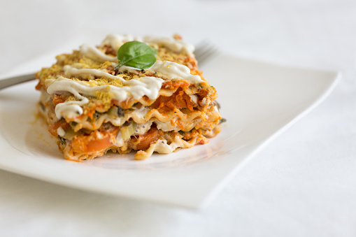 Vegan lasagna with vegetables, tomato sauce, cashew sauce and garnished with fresh basil and nutritional yeast.