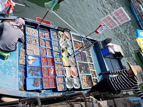 Local men selling fresh fish and seafood directly from the boats in Sai Kung Town harbor, a town on Sai Kung Peninsula, in the New Territories, Hong Kong.