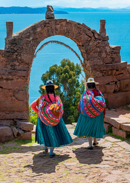 Quechua People, Titicaca Lake, Peru Two Peruvian Quechua indigenous women in traditional clothes walking through the arch of the rulers on Taquile island with the Titicaca Lake in the background, Peru. peruvian culture photos stock pictures, royalty-free photos & images