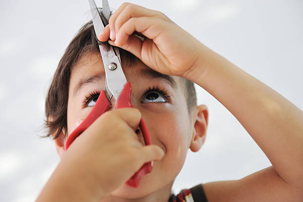 Young boy looking up at scissors while cutting own hair stock photo