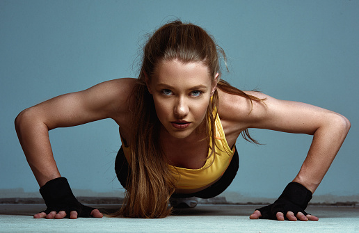 Determined and fit blonde woman doing push-ups in the gym, looking at the camera, feeling attractive and sporty
