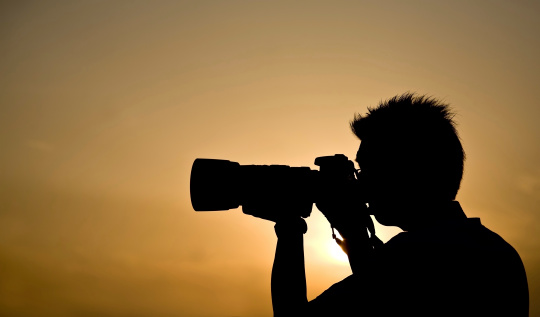 Silhouette of a photographer holding a telephoto lens