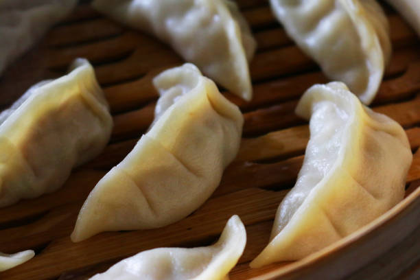 Close-up image of Momos (South Asian dumplings), white flour and water dough filled with chicken and mixed vegetables in bamboo steamer being cooked, elevated view Stock photo showing a restaurant meal of steaming dumplings (Momos) filled with mixed vegetables and chicken in bamboo steamer. chinese dumpling photos stock pictures, royalty-free photos & images