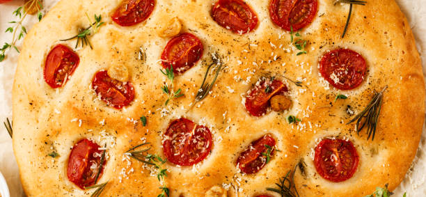 italienische traditionelle focaccia brot backen mit kirschroten tomaten, parmesan und rosmarin auf hellbraunem hintergrund. ansicht von oben. - italian cuisine gluten free food tomato herb stock-fotos und bilder