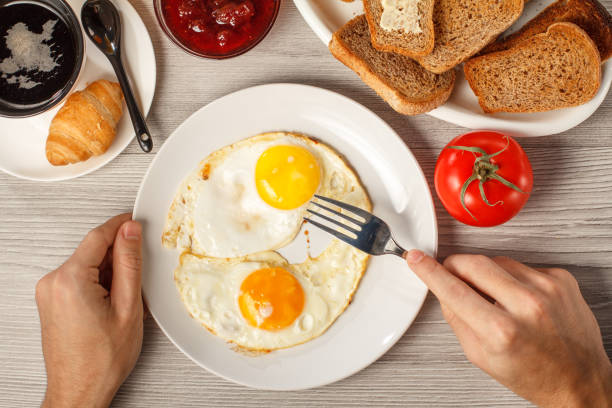 istock Male hands holding plate with fried eggs and fork at the desk 1229664964