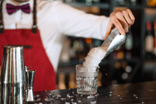 istock Bartender in the white shirt adding ice into cocktail glass on the bar counter 1229683130