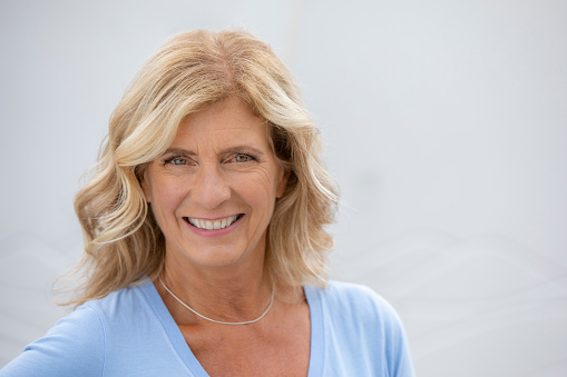 Headshot of mature woman with blond hair with white background.