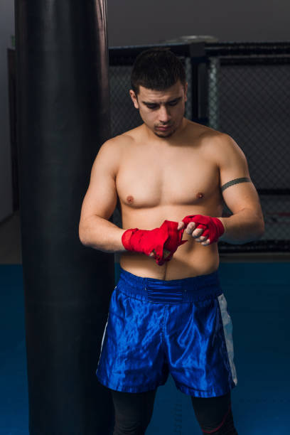 istock Young boxer wrapping his hands with red elastic bandage preparing to workout 1229774915