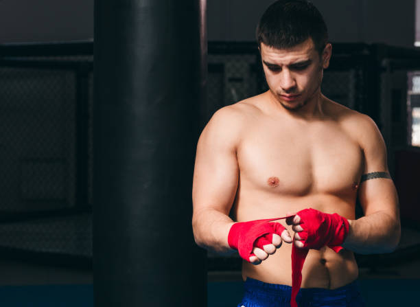 istock Young boxer wrapping his hands with red elastic bandage preparing to workout 1229775359