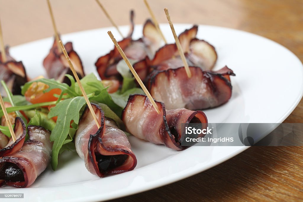 Bacon bits on a stick with prunes Baked prunes in bacon on a plate with salad Dried Plum Stock Photo