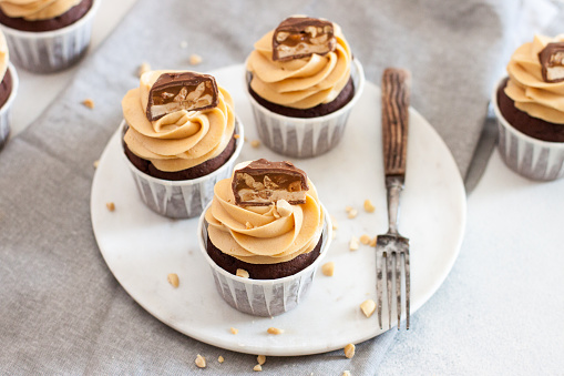 Peanut butter cupcakes with chocolate bites and chopped nuts on grey linen tablecloth. Chocolate dough and mascarpone frosting.