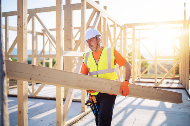 Builder Working On Wooden House Side view of builder holding wooden beam, working on unfinished wooden house at sunset. building contractor stock pictures, royalty-free photos & images