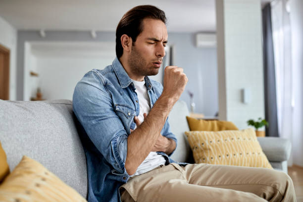 istock Young man coughing while sitting in the living room. 1229984033