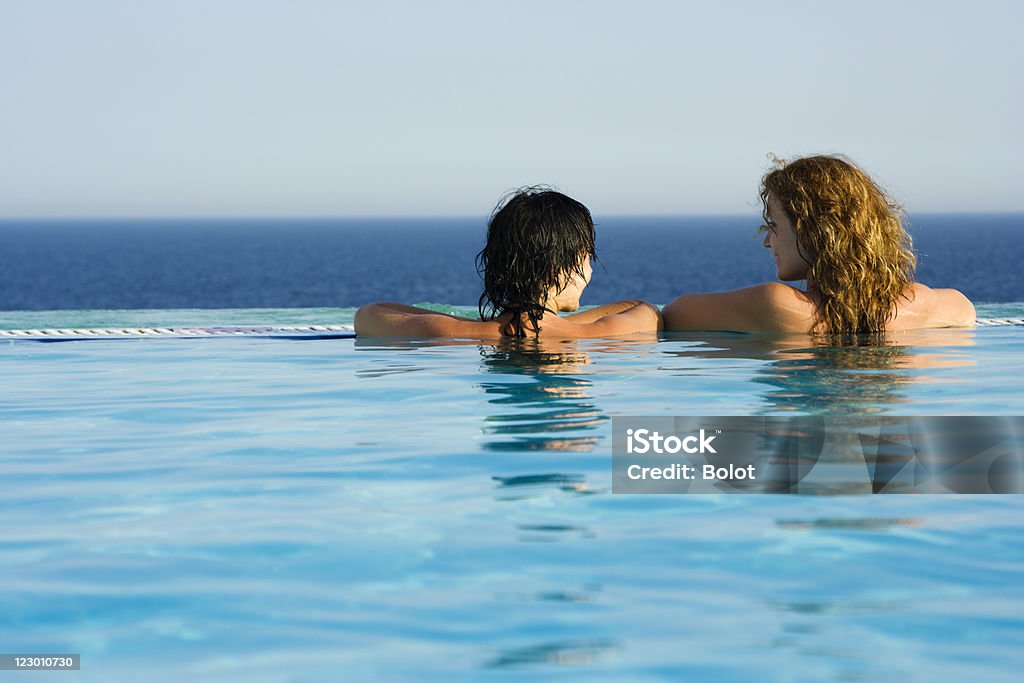 Dos mujeres jóvenes en la piscina de borde infinito - Foto de stock de Actividades recreativas libre de derechos