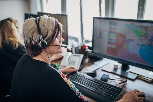 Young beautiful woman casual dressed in headsets is listening to a company's client, while she is sitting at the desk, working together with a male colleague in a modern office. Focus on woman. Call center operators at work.