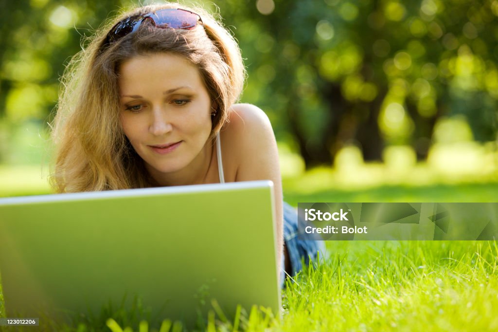 Mujer joven usando una computadora portátil en el parque - Foto de stock de Acostado libre de derechos