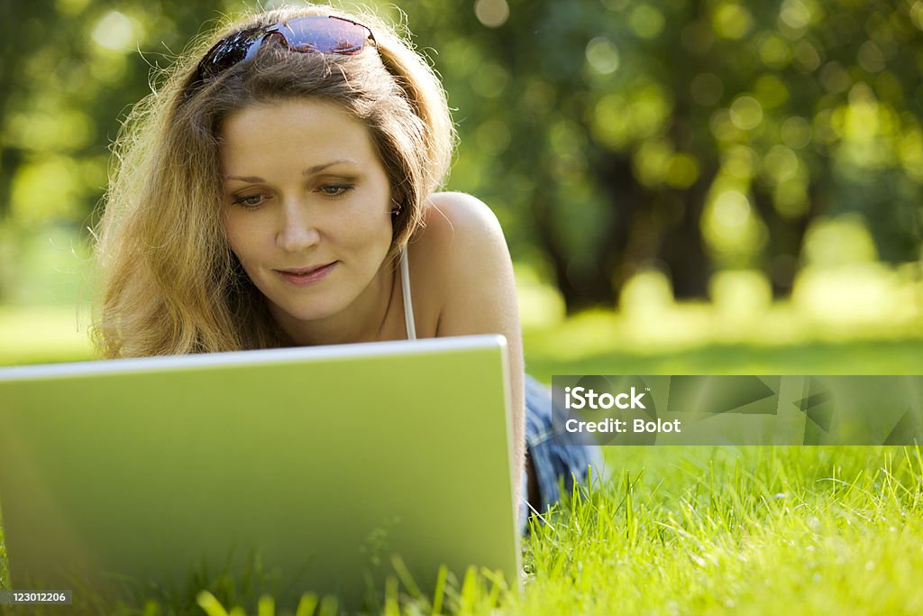 Młoda kobieta za pomocą laptopa w parku - Zbiór zdjęć royalty-free (Brązowe włosy)