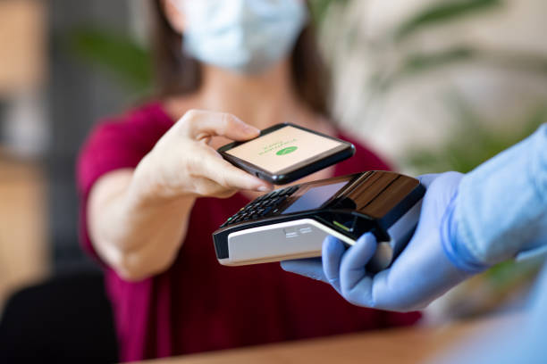 Contactless smartphone payment Close up hand of customer paying with smartphone. Cashier hand holding credit card reader machine and wearing protective disposable gloves at bar counter, while client holding phone for NFC payment. Woman wearing face mask while paying bill with mobile phone during Covid-19 pandemic. cashier photos stock pictures, royalty-free photos & images
