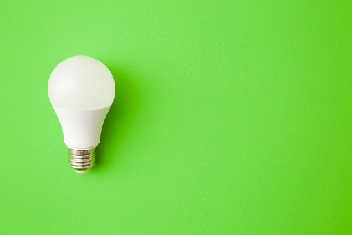 One white led light bulb on bright green table background. Closeup. Energy saving. Empty place for text or logo. Top down view.