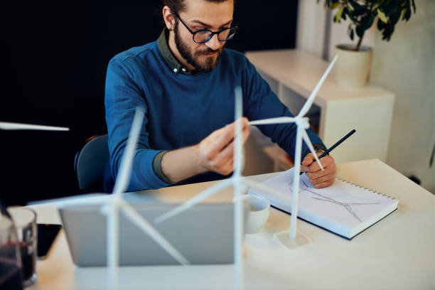 istock Attractive bearded environmentalist sitting in his office and drawing new windmill model. 1230386141