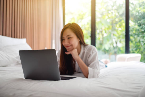 istock woman using and working on laptop computer while lying down on a white cozy bed at home 1230396617