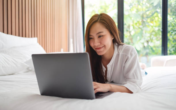 istock woman using and working on laptop computer while lying down on a white cozy bed at home 1230397918