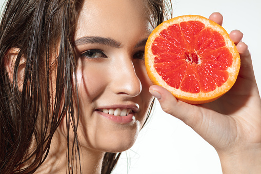 Summer. Close up of beautiful young woman with big grapefruit on white background. Concept of cosmetics, makeup, natural and eco treatment, skin care. Shiny and healthy skin, fashion, healthcare.