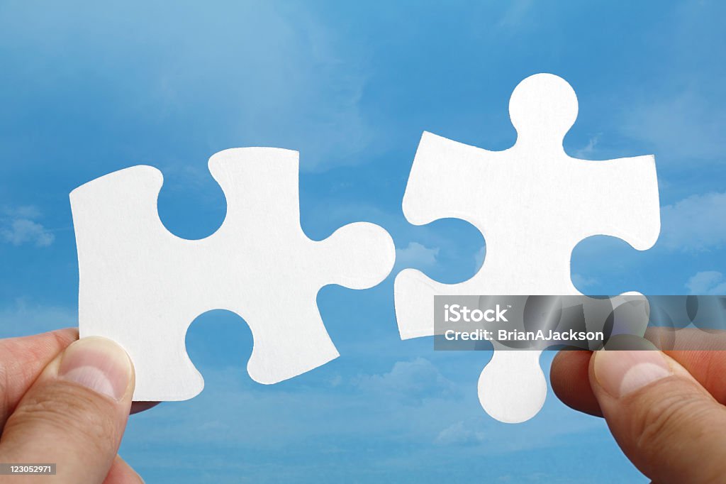 Fingers holding two pieces of a puzzle that fit together Holding two jigsaw pieces of a blank puzzle trying to fit together against blue sky background Jigsaw Piece Stock Photo