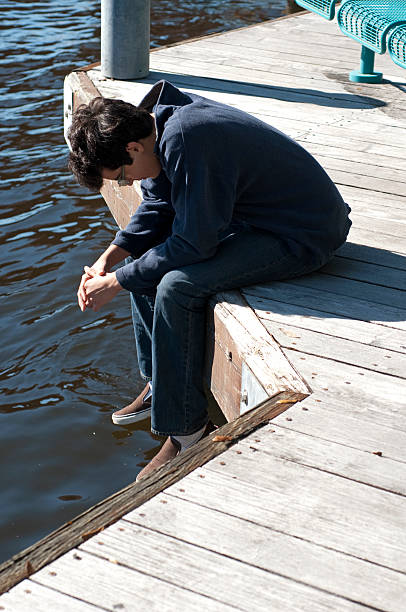 A peaceful scene as a mid-adult man sits by the tranquil lakeside, soaking in the breathtaking sunset view. The warm hues of the sky reflect on the calm water, creating a serene and contemplative moment.
