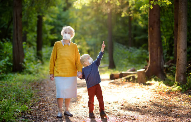 grand-mère âgée et petit-enfant portant le masque de visage marchant ensemble dans le stationnement ensoleillé d’été. grand-mère et petit-fils. levée des ordres de verrouillage du virus. distanciation sociale. - senior adult human face male action photos et images de collection