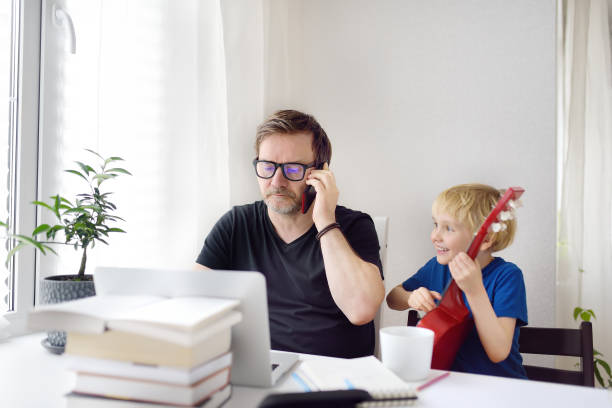 istock Man working from home with laptop during quarantine. Home office and parenthood at same time. Exhausted parent with hyperactive child. 1230585446