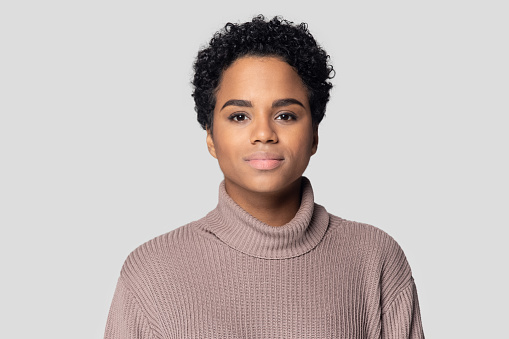 Head shot portrait African young woman having short black hairs wears knitted sweater posing isolated on gray background, serious beautiful 20s mixed-race girl look at camera, natural beauty concept