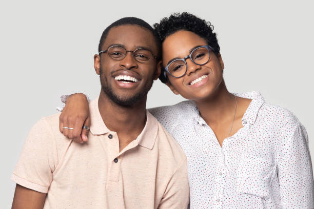 African couple embracing smiling looking at camera posing on grey Head shot portrait African attractive married couple in glasses embracing smiling looking at camera posing isolated on grey background, love and relations, clients of photo shooting in studio concept teeth bonding stock pictures, royalty-free photos & images