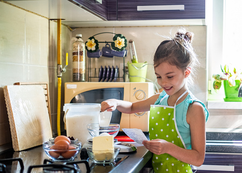 Smiling girl reading recipe and making a cake