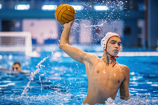 Young man playing a water polo game in the indoor pool.