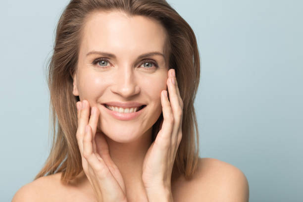 Head shot portrait smiling woman touching perfect smooth face skin Head shot portrait smiling woman touching perfect smooth face skin, looking at camera, attractive young female with bare shoulders, natural beauty concept, close up isolated on studio background toned image stock pictures, royalty-free photos & images