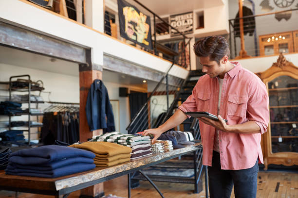 mężczyzna właściciel sklepu mody za pomocą cyfrowego tabletu, aby sprawdzić zapasy w sklepie odzieżowym - clothing store sales clerk usa clothing zdjęcia i obrazy z banku zdjęć