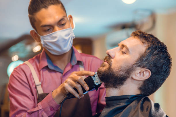 istock Beard styling. Barber shaping beard of handsome man using a trimmer. Skilled barber trimming beard to his client 1230835509