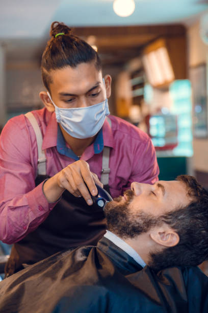 Beard styling. Barber shaping beard of handsome man using a trimmer. Skilled barber trimming beard to his client