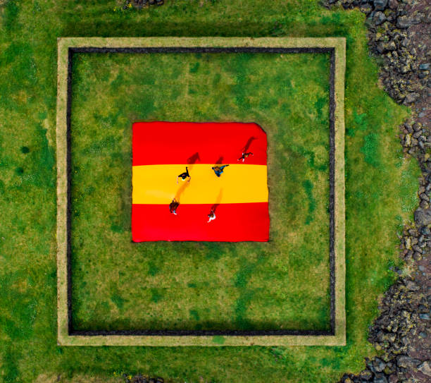 Six persons with some distance between them standing on the Spanish flag